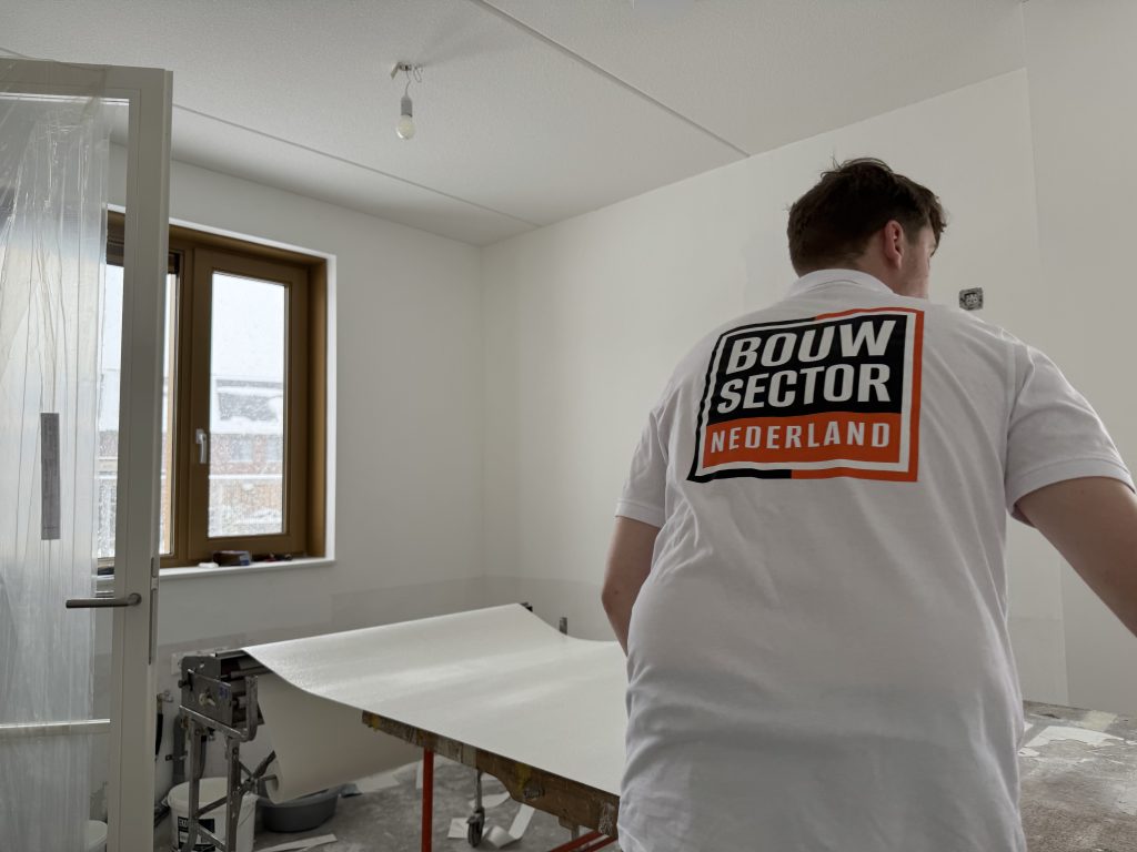 Behanger van Bouwsector Nederland in wit poloshirt rolt een baan renovlies uit over de plaktafel