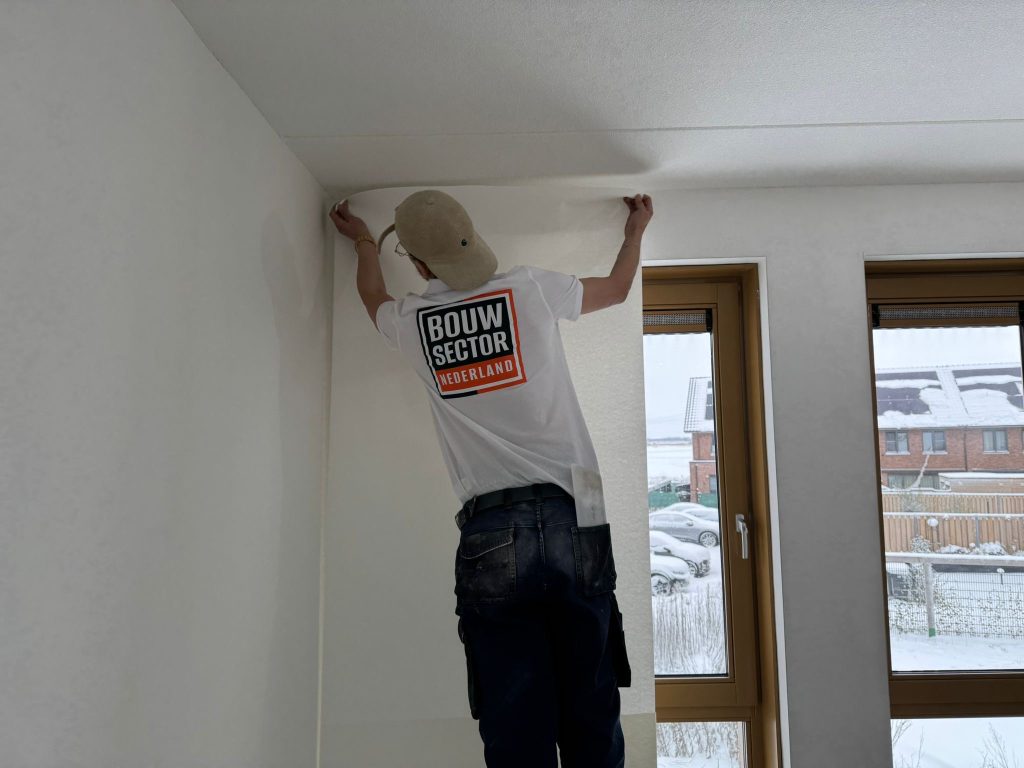 Behanger van Bouwsector Nederland zet een baan renovlies bovenaan tegen het plafond