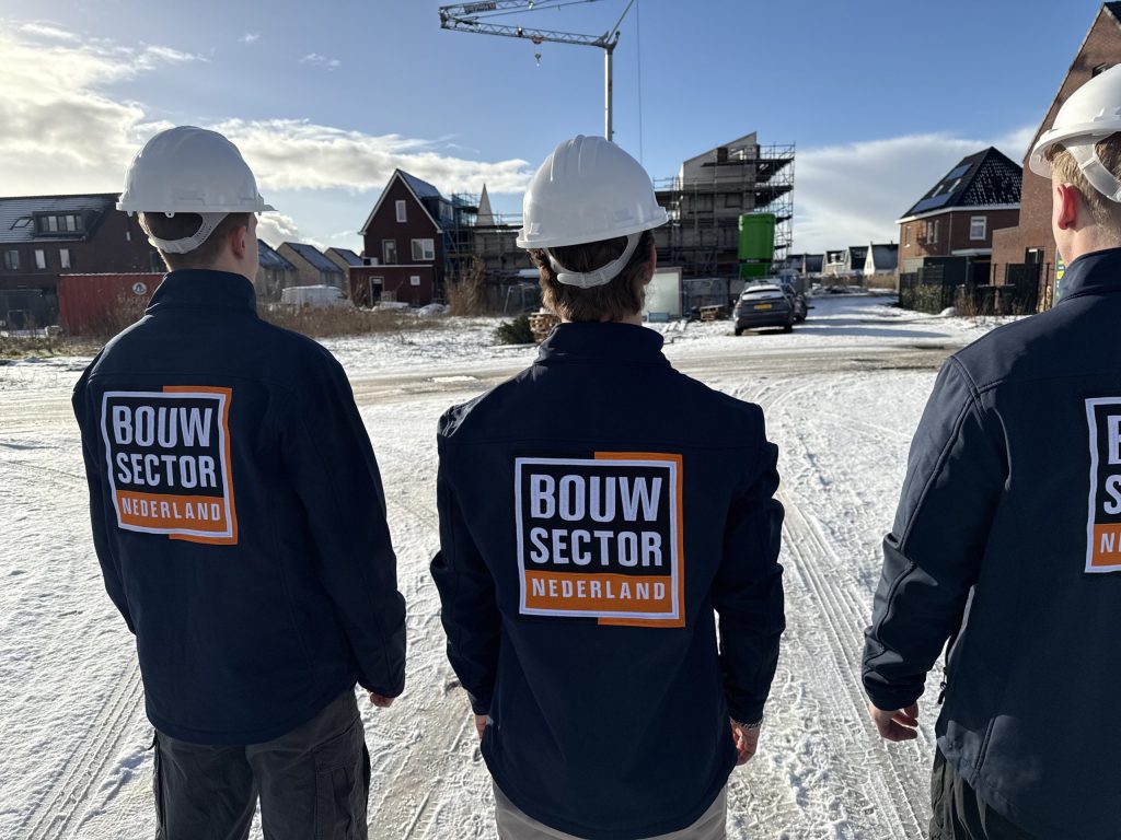Drie vakmensen van Bouwsector Nederland met witte helm kijken naar nieuwe huizen in aanbouw